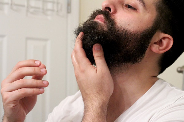 мужчина наносит масло на бороду