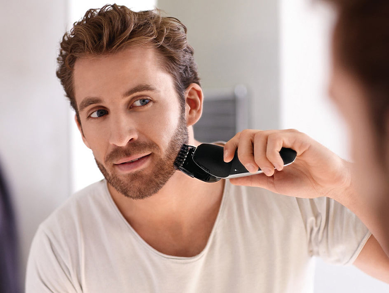 мужчина бреется машинкой для стрижки бороды